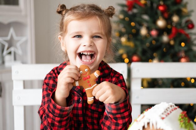 niñita en pijama rojo sosteniendo una galleta de hombre de jengibre de Navidad decorada