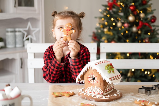 niñita en pijama rojo sosteniendo una galleta de hombre de jengibre de Navidad decorada