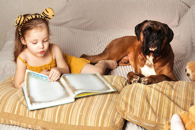 niñita en el sofá de casa con su gran perro rojo, leyendo un libro