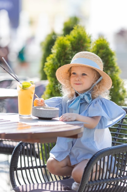 niñita con sombrero de paja y vestido azul está desayunando al aire libre