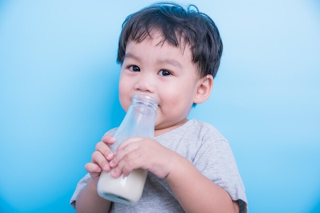 Un niñito asiático bebiendo leche de una botella de vidrio con fondo azul