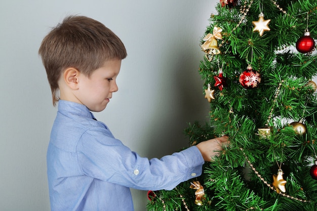 Niñito decorar el árbol de Navidad con adornos en la habitación