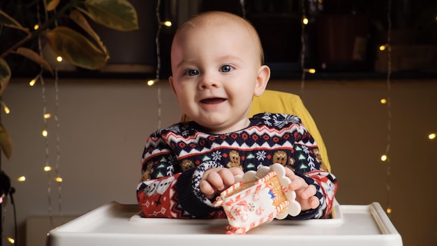 Un niñito con suéter navideño sonriendo jugando con una casa de pan de jengibre de juguete