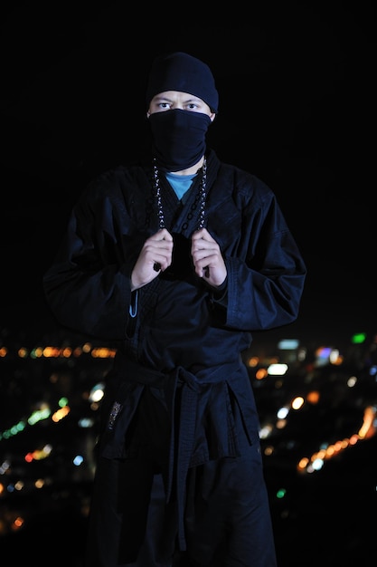 Ninja assassino segurar katana samurai velha arma marcial swordat noite com luzes da cidade em segundo plano