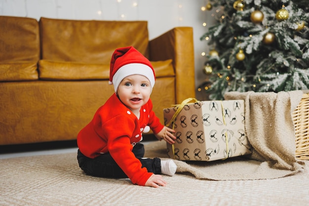 Un niño de 1 año se sienta en una canasta contra el fondo de un árbol de Navidad Un niño en un viento rojo de Año Nuevo cerca del árbol de Navidad