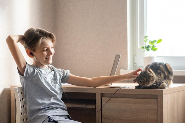 Un niño de 11 años está sentado en una mesa en su habitación escuchando música con auriculares