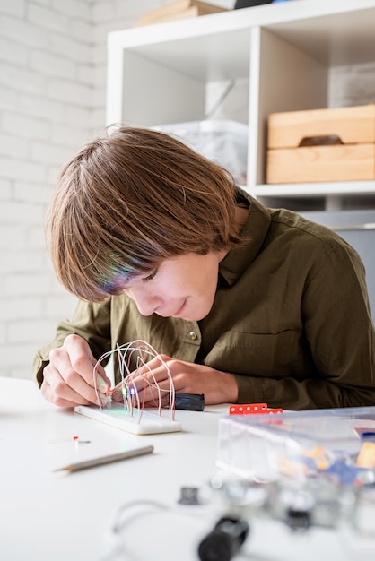 Niño de 12 años construyendo un coche robot sentado a la mesa jugando con luces