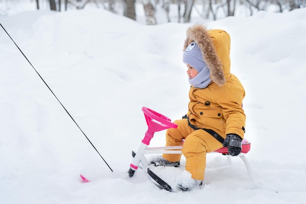 A un niño de 1223 meses le gusta montar un snowcat en la nieve en una vista lateral del parque de invierno
