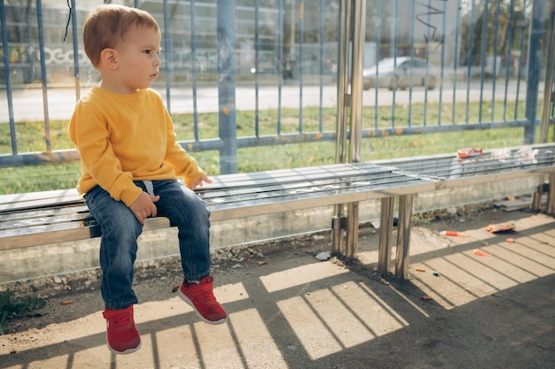 niño de 2-3 años se sienta en una parada de autobús y espera el transporte