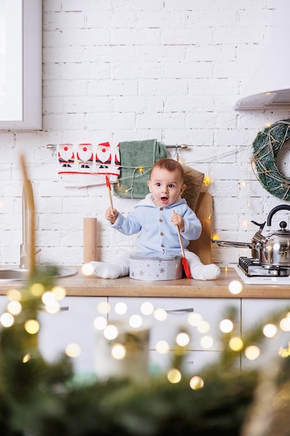 Un niño de 2 años está sentado en la cocina decorado con adornos navideños.