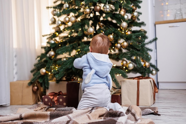 Un niño de 2 años se sienta cerca de un árbol de Navidad decorado con juguetes Ambiente de Año Nuevo