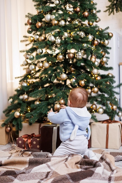 Un niño de 2 años se sienta cerca de un árbol de Navidad decorado con juguetes Ambiente de Año Nuevo