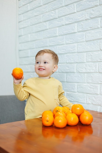 Un niño de 2 años tiene mandarinas en sus manos. El niño quiere sentarse en frutas cítricas por primera vez.