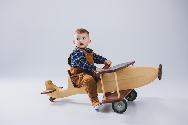 Un niño de 3 años con una camisa a cuadros se sienta en un gran avión de madera Juguetes de madera ecológicos para niños