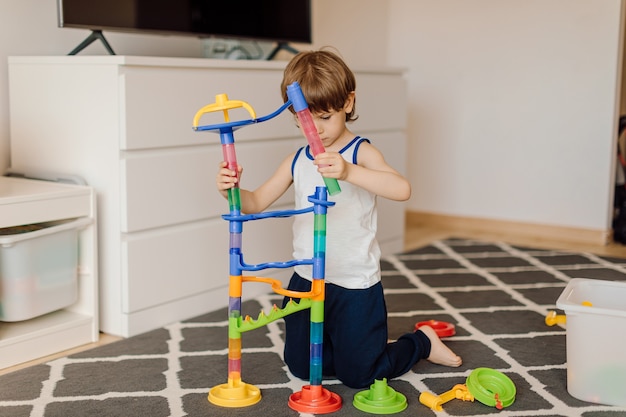 Niño de 3 años está construyendo una construcción de plástico sentado en el piso de la casa. Concepto de soledad y niños con problemas de autismo.