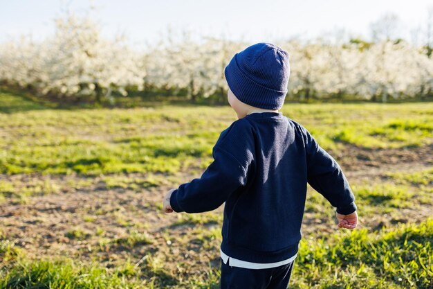 Un niño de 3 años con un suéter y un sombrero corre por un jardín  floreciente ropa para niños de 3 años un niño eotiano feliz es blanco entre  manzanos en flor