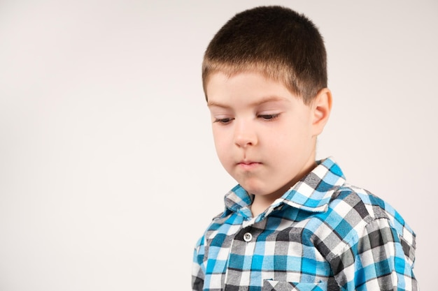 Foto un niño de 4 años con una camisa azul a cuadros mira hacia abajo