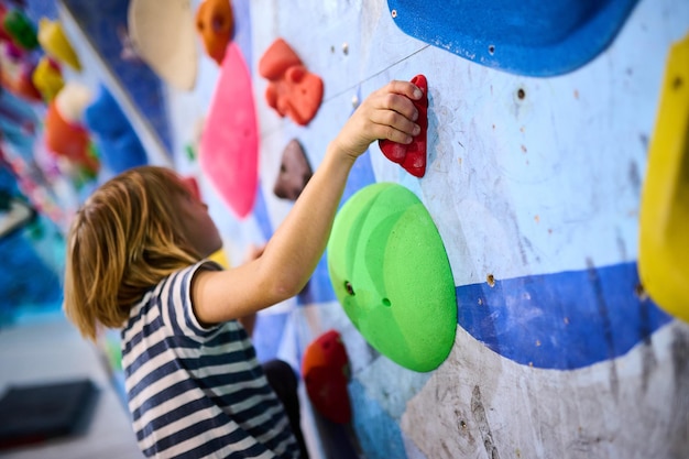 Un niño de 6 años se centró en escalar cuidadosamente agarrando pequeñas garras en una pared de roca interior las garras coloridas y la concentración detallada muestran su determinación
