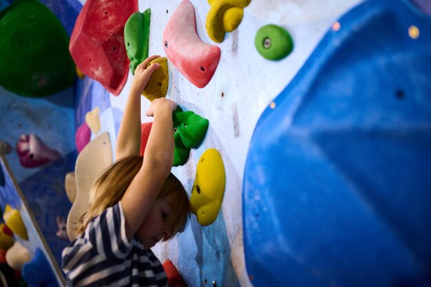 Un niño de 6 años se centró en escalar cuidadosamente agarrando pequeñas garras en una pared de roca interior las garras coloridas y la concentración detallada muestran su determinación