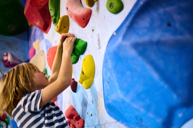 Un niño de 6 años se centró en escalar cuidadosamente agarrando pequeñas garras en una pared de roca interior las garras coloridas y la concentración detallada muestran su determinación