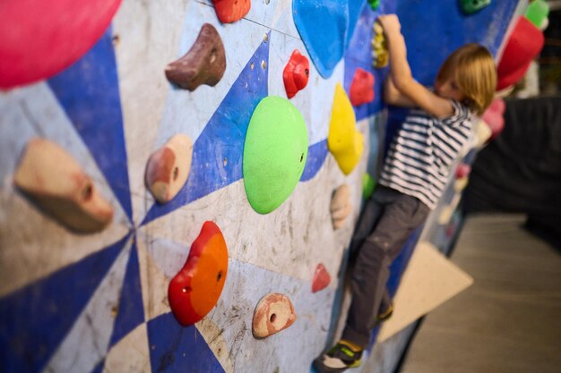 Un niño de 6 años escalando en una vibrante pared de roca interior con sujetos multicolores participando en una experiencia de escalada divertida y activa perfecta para niños de fitness y aventura