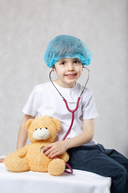 Niño de 6 años vestido con gorro médico desechable examina osito de peluche