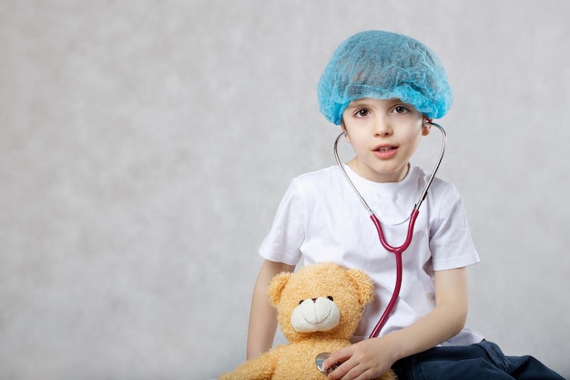 Niño de 6 años vestido con gorro médico desechable examina osito de peluche