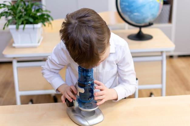 Un niño de 7-8 años con camisa blanca mira a través de un microscopio. Foto de alta calidad