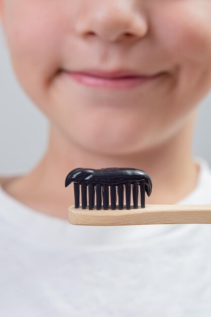 Un niño de 7 años sin un diente de leche se cepilla los dientes con un cepillo de bambú y pasta de dientes negra.