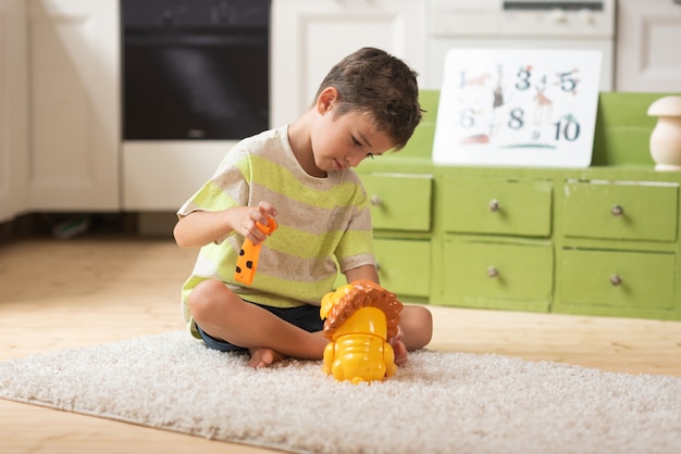 Un niño de 7 años se sienta en la alfombra y juega con juguetes en casa Juegos educativos