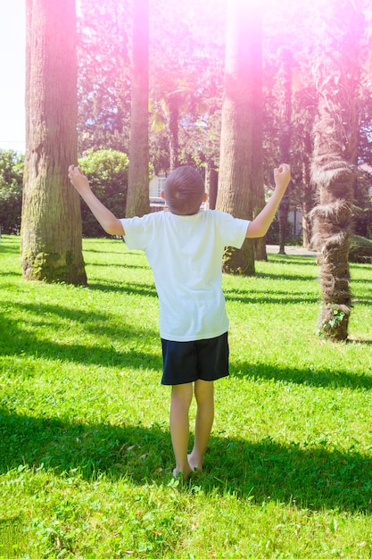 Niño de 7 años tira de las manos al sol haciendo yoga y mira hacia arriba a las palmeras vista trasera Sueño y meditación zen como concepto Relajación viajes vacaciones niños