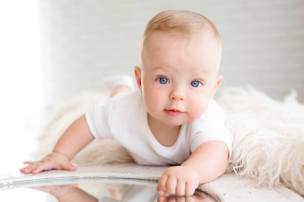 Niño de 7 meses juega en la alfombra blanca del dormitorio con un espejo