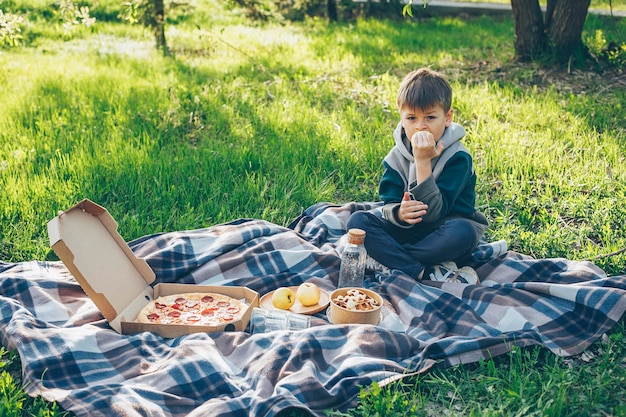 Niño de 78 años sentado en cuadros escoceses y comiendo manzana Concepto de picnic de primavera o verano