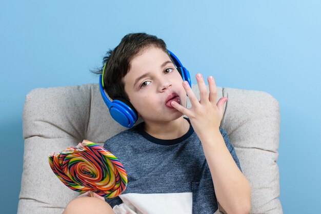 Niño de 8 años con auriculares y sosteniendo una paleta de colores y lamiendo sus dedos.