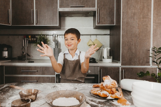 Niño de 8 años en la cocina juega con harina. niño en la cocina prepara masa.