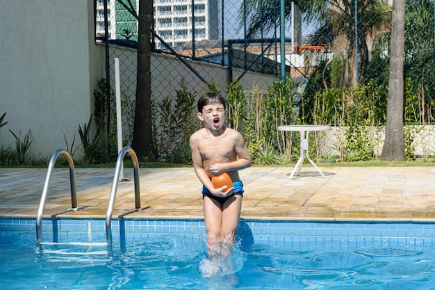 Niño de 8 años haciendo una mueca y zambulléndose en la piscina con una bomba de agua.