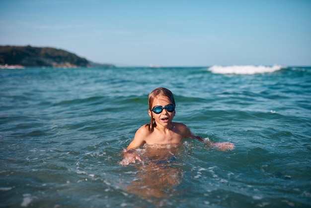 Niño de 8 años nada en el mar con gafas de natación azules por la noche