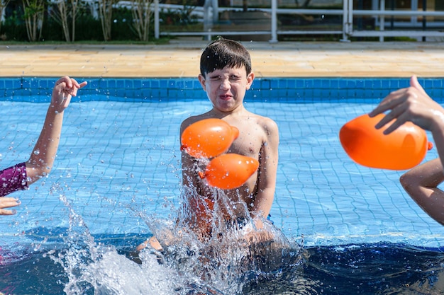 Niño de 8 años sentado en el borde de la piscina, jugando con varias bombas de agua.