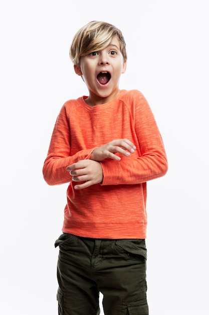 Un niño de 9 años con un suéter naranja y jeans grita asustado. Fondo blanco. Vertical.