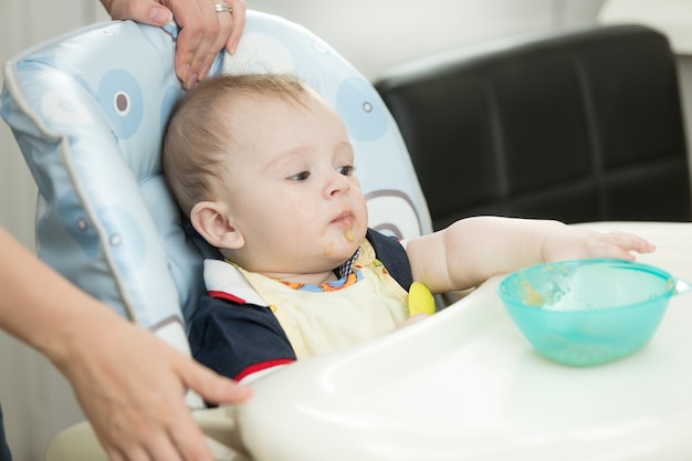 Niño de 9 meses sentado en una trona y alcanzar el plato