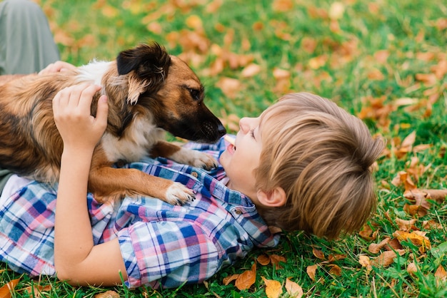 Niño abrazando a un perro y jugando con en el otoño, parque de la ciudad