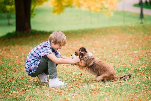 Niño abrazando a un perro y jugando con en el otoño