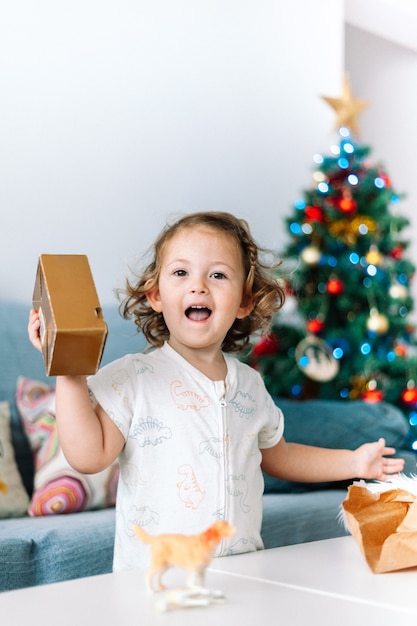 Niño abriendo regalos de Navidad en pijama junto al árbol de Navidad