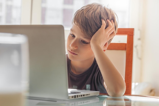 Niño aburrido usando computadora portátil en la mesa en casa
