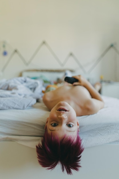 Foto un niño aburrido viendo la televisión desde la cama durante las vacaciones