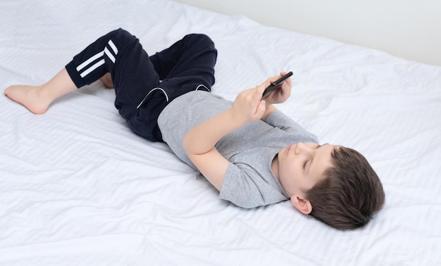 Niño acostado en la cama con un teléfono inteligente jugando o estudiando algo en él