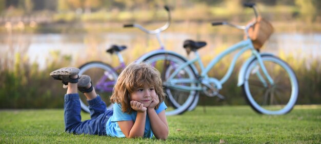 Niño acostado en la hierba en el retrato del parque de verano de un niño sonriente acostado en la hierba verde ou