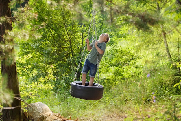 Niño activo en un colorido neumático de columpio casero en el bosque. Actividad de verano saludable para niños.