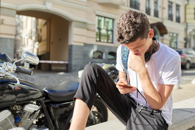 Niño adolescente de 1617 años usando un teléfono inteligente sentado en la calle de la ciudad de verano