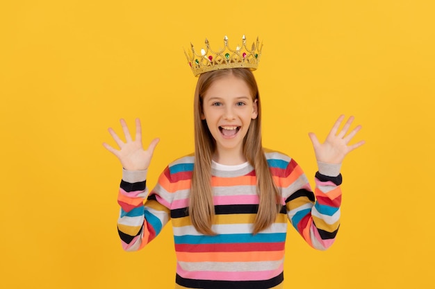 Niño adolescente alegre en la corona de la reina sobre fondo amarillo